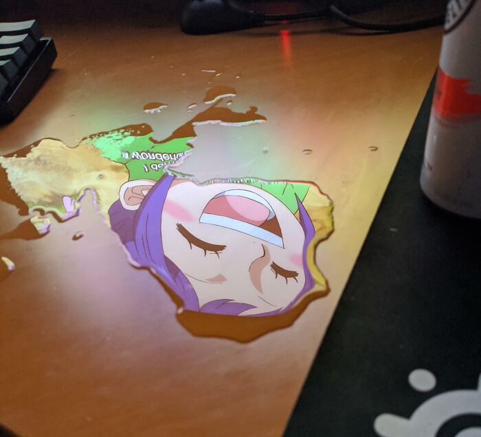 A puddle on a desk reflecting an anime character; real scene looks fake at first glance.
