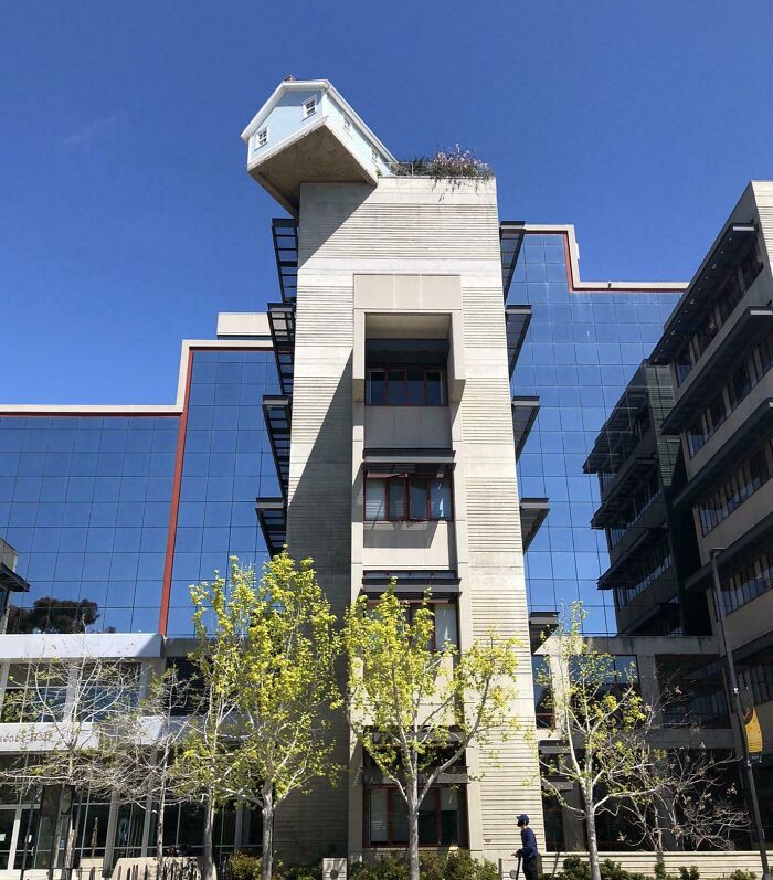 House atop building tower against blue sky, real but appears fake.