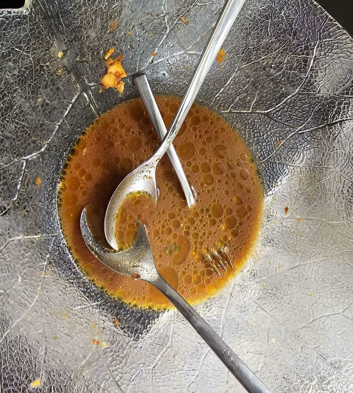 Spoons and fork in a dish with leftover soup, creating an optical illusion that looks fake but is real.