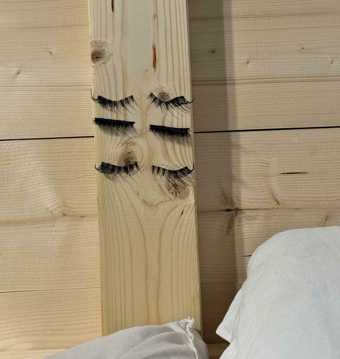 Wooden board with false eyelashes, humorously styled to resemble a face, showing a man's playful creativity.
