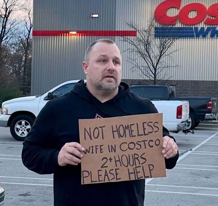 Man holding a funny sign outside Costco, humorously highlighting life with entertaining partners.