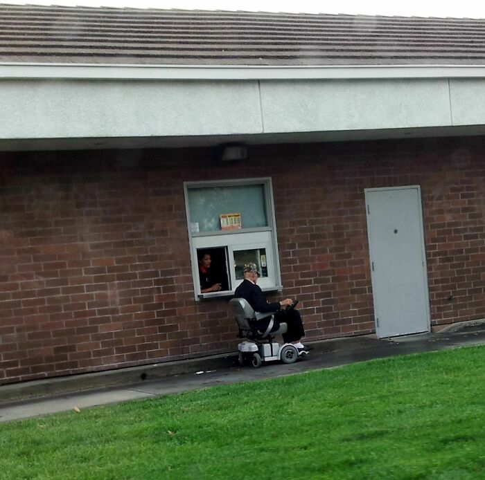 Elderly person in a mobility scooter at a drive-thru window, demonstrating humor and playfulness.
