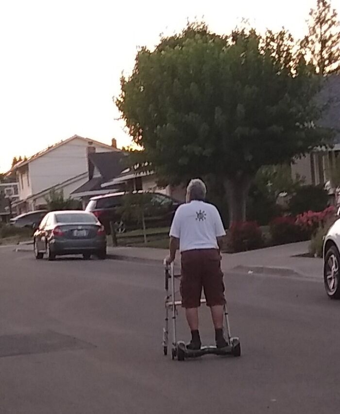 Elderly person humorously using a walker on a hoverboard in a suburban street at sunset.