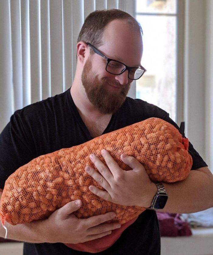A man smiling, holding a large bag of peanuts, wearing glasses and a black shirt, exudes a humorous and playful vibe.