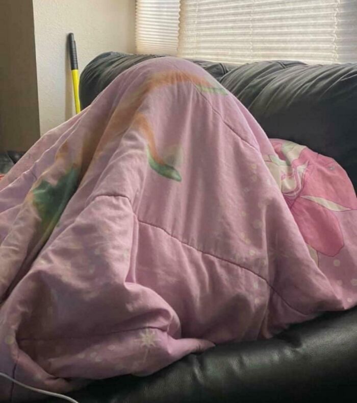 A person humorously hiding under a pink blanket on a couch, showcasing a funny moment with their partner.