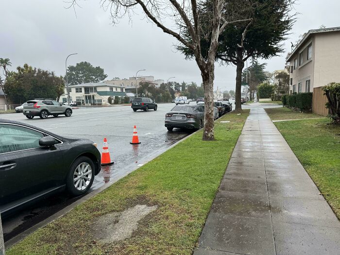 Poor parking etiquette with a car blocking road cones on a rainy street.