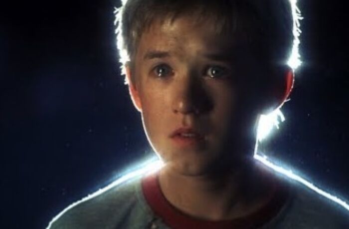 Young boy gazing forward with tears in his eyes, backlit in a dim scene, evoking emotional movie moments.