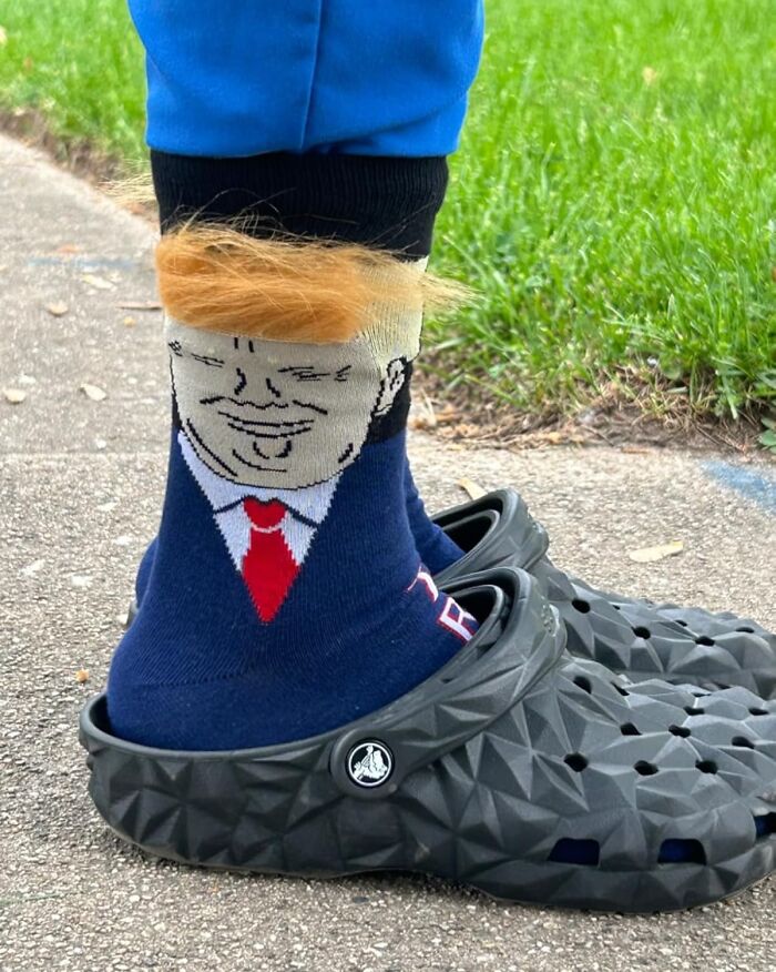 Quirky socks with a cartoon face and fuzzy hair, worn with black Crocs on a sidewalk.