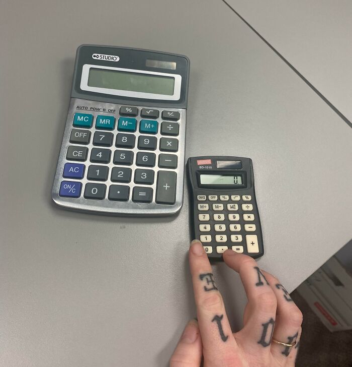 Hand holding a tiny calculator next to a large one on a desk, highlighting infuriating bosses with unfair resources.