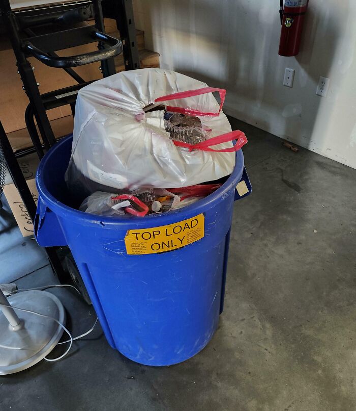 Overfilled trash can with "Top Load Only" sign, highlighting poor management decisions by infuriating superiors.