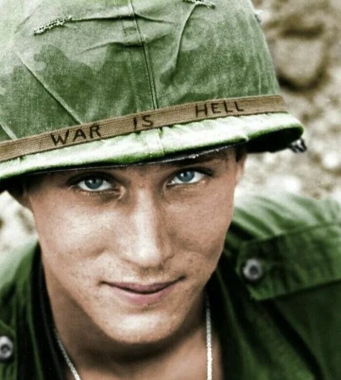 Close-up vintage photo of a soldier wearing a helmet with "War is Hell" written, showing history up close and personal.