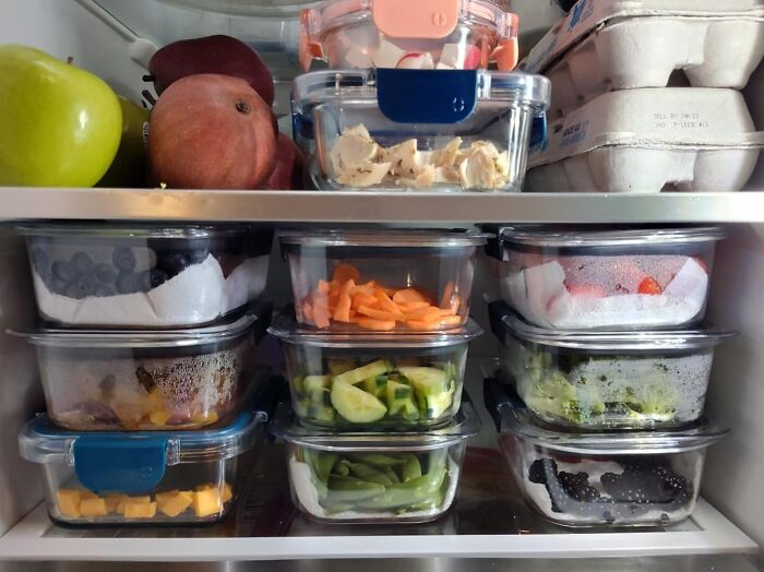 Meal prep containers filled with assorted fruits and vegetables in a refrigerator.