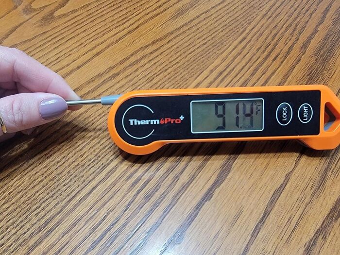 A meat thermometer, an essential meal prep item, displaying a temperature of 91.9°F on a wooden table.