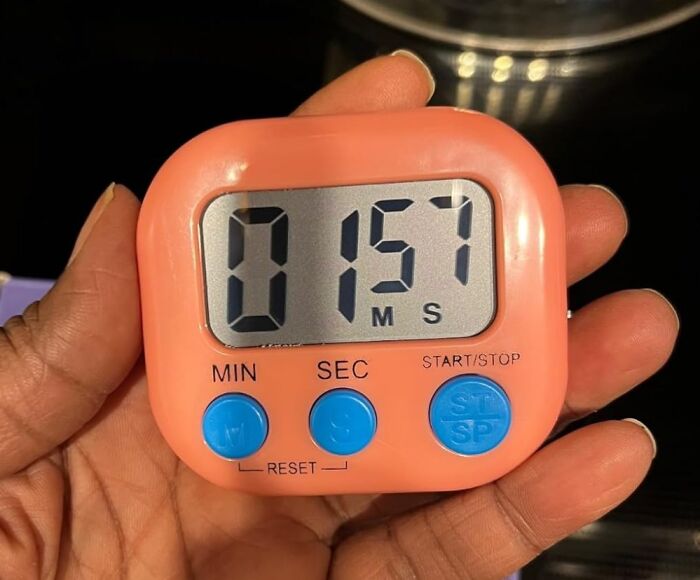 Hand holding a pink kitchen timer, a helpful tool for meal prep efficiency.