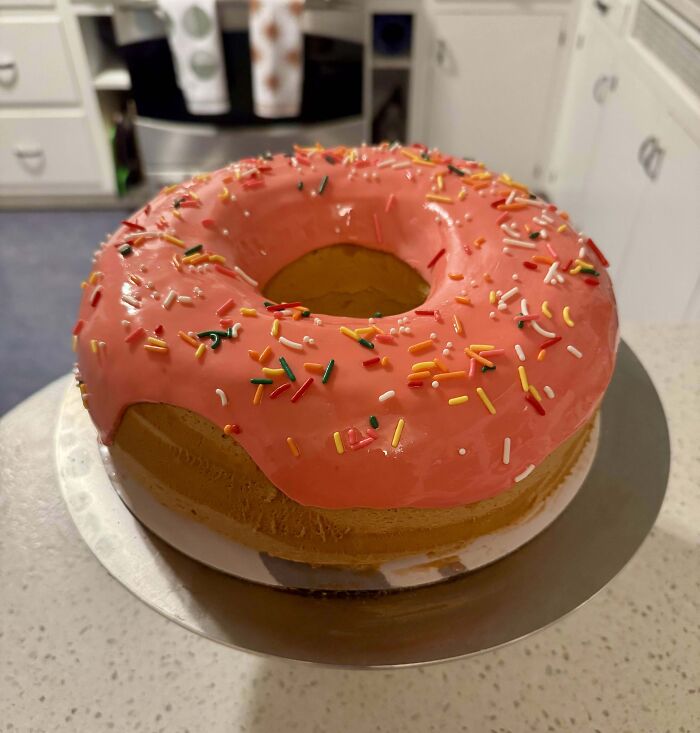 Giant donut-shaped cake with pink icing and sprinkles, showcasing a unique culinary concoction on a countertop.