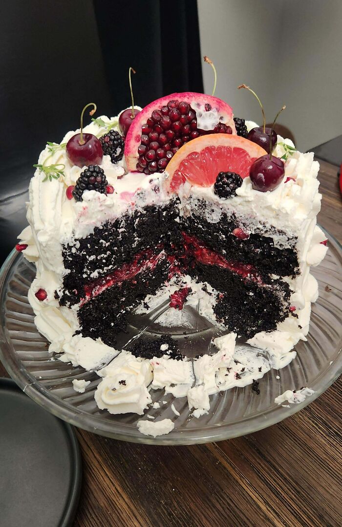 Culinary confection: A layered chocolate cake with berries, topped with grapefruit and pomegranate slices on a glass plate.
