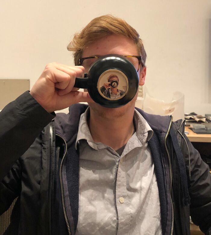 Man humorously sips from cup, reflection creates funny coworker moment deserving a raise for creativity.
