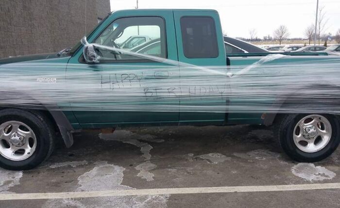 Funny coworkers wrap a truck in plastic wrap with "Happy Birthday" written on it in a parking lot.