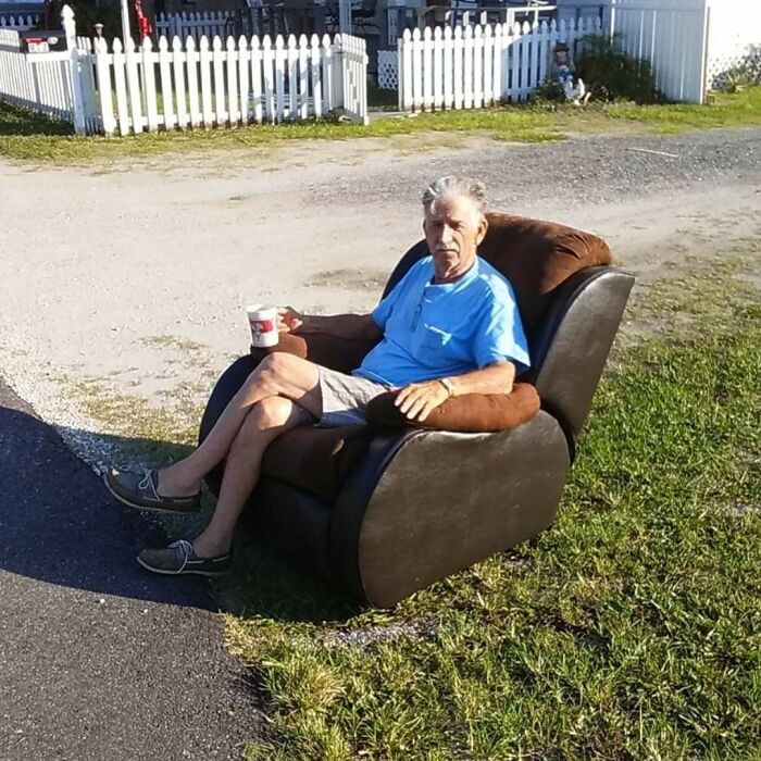 Elderly man sitting humorously in a recliner outdoors, holding a drink in a relaxed setting.