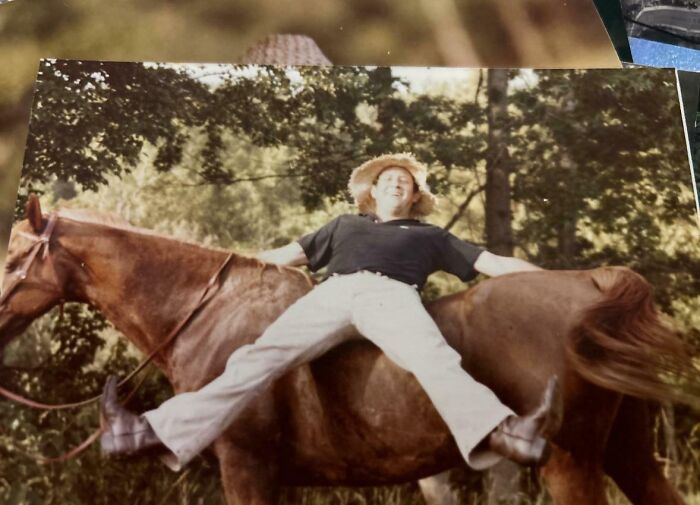 Elderly person humorously riding a horse backward, wearing a straw hat and smiling outdoors.