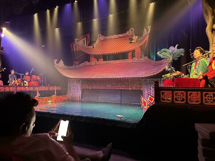 Audience member on phone during a cultural performance, demonstrating a lack of basic etiquette.