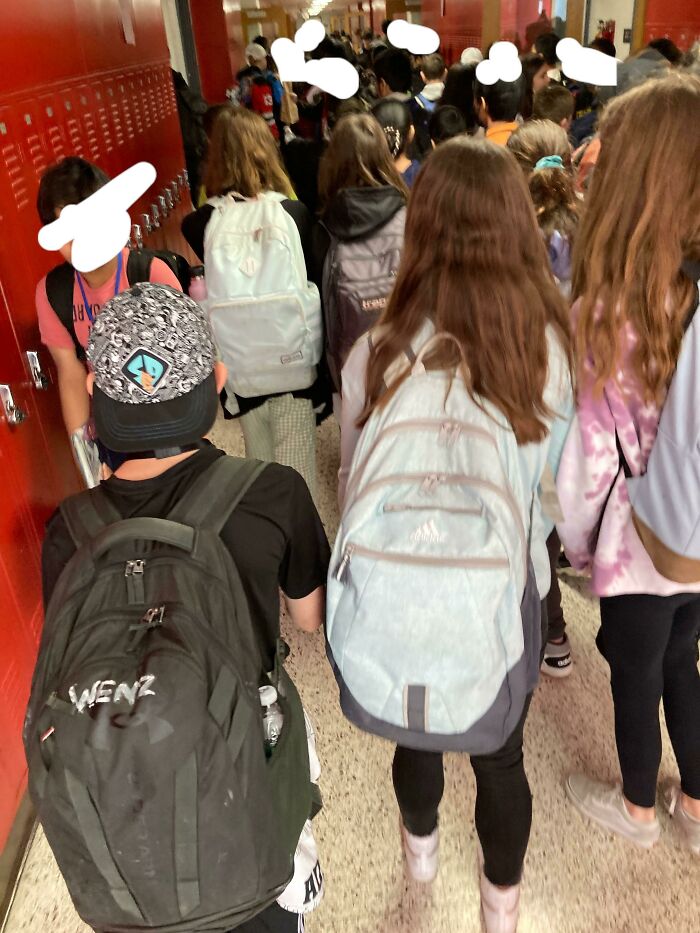 Students with backpacks walking through a crowded American school hallway.