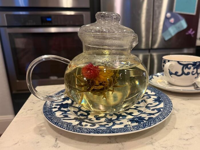 Glass teapot with blooming tea, set on a decorative blue plate, perfect for Easter basket treats.