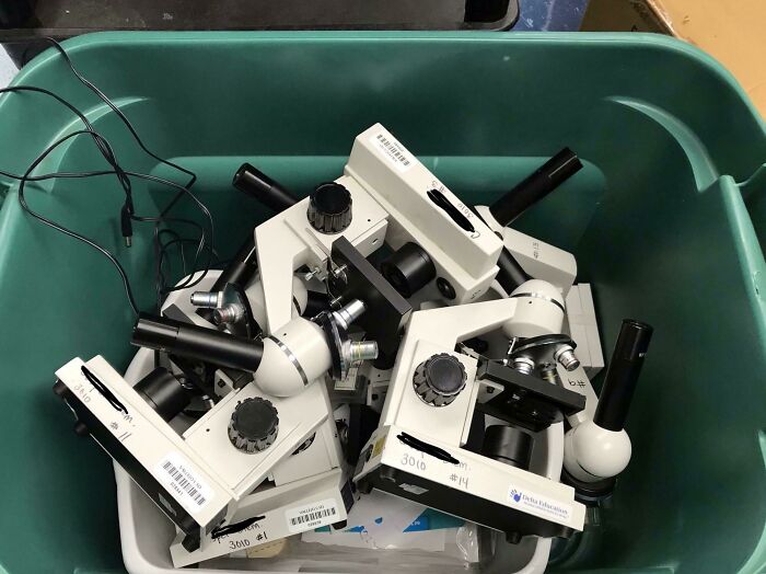Microscopes piled in a green container, highlighting American schools' equipment issues.