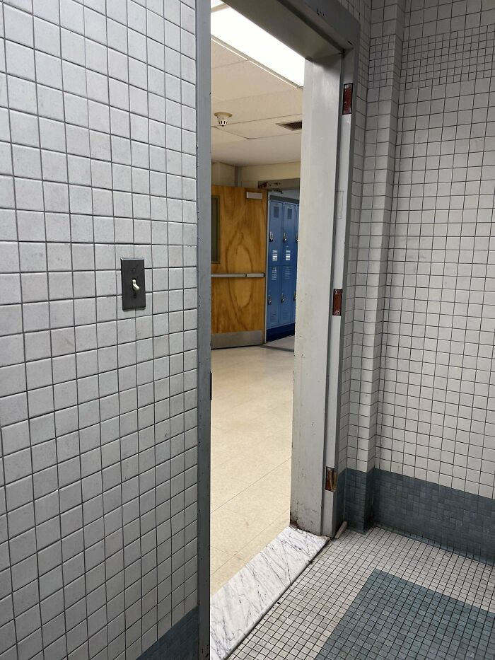 Open door in a tiled hallway revealing American school lockers and a wooden door.