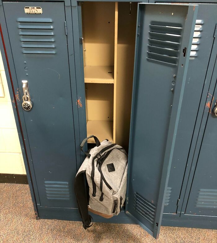 A gray backpack partially inside a blue school locker with a combination lock.