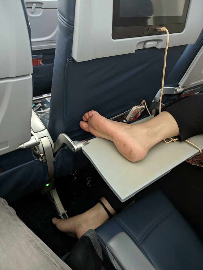 Bare feet on airplane seatback tray, showcasing lack of basic etiquette.