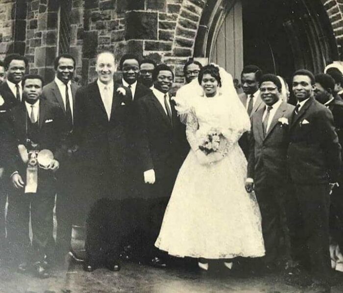 Vintage wedding photo of a bride and groom with guests in front of a church, showcasing timeless love and style.
