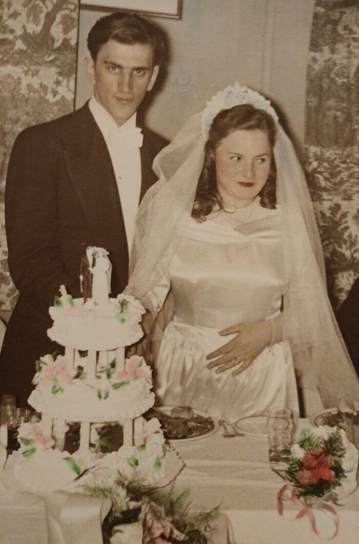 Bride and groom stand beside a tiered wedding cake, showcasing vintage wedding style with classic attire.