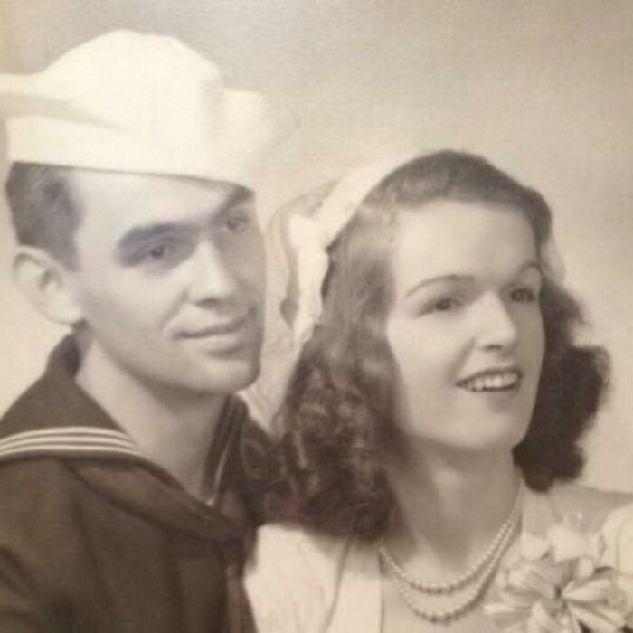 Vintage wedding photo of a couple smiling, man in a sailor uniform, woman with curls and pearls, evoking timeless love.