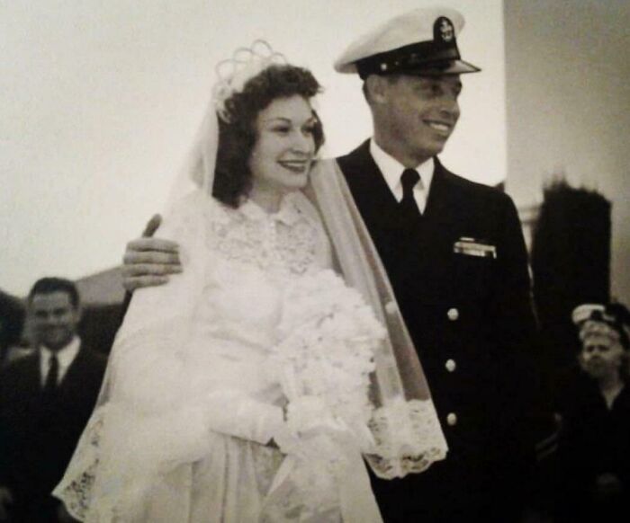 Vintage wedding photo of a smiling couple, bride in classic gown and groom in navy uniform, celebrating love timelessly.