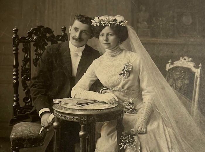 Vintage wedding photo of a couple seated at a small table, with the bride wearing a floral headdress and lace gown.