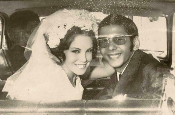 Smiling couple in a classic car on their wedding day, showcasing vintage love style.