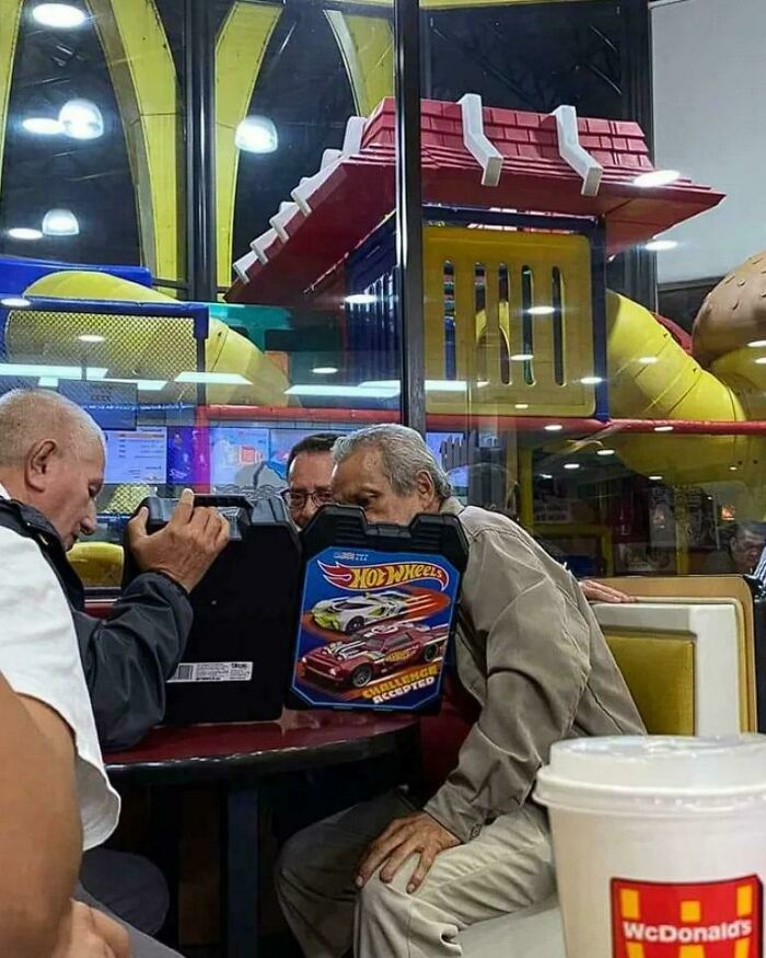 Elderly people at McDonald's playfully looking at Hot Wheels toy case, demonstrating their humorous side.