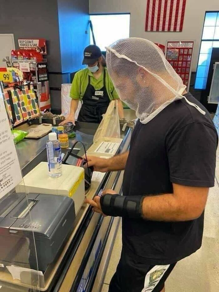 Person wearing a mesh head cover at a store checkout, with a flag and cashier in the background.