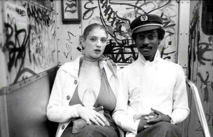 Two people sitting in a graffiti-covered subway, one wearing a uniform; a glimpse into historical moments.