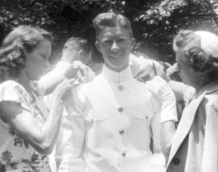 Young man in military uniform getting help from women, capturing a moment in historical fashion.