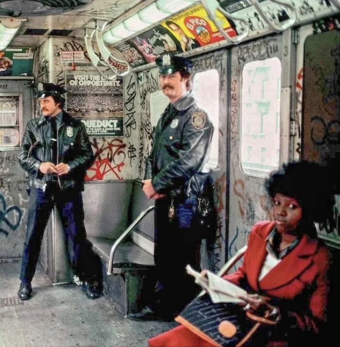 Vintage subway scene with two police officers and a woman reading, surrounded by graffiti, capturing historical urban life.