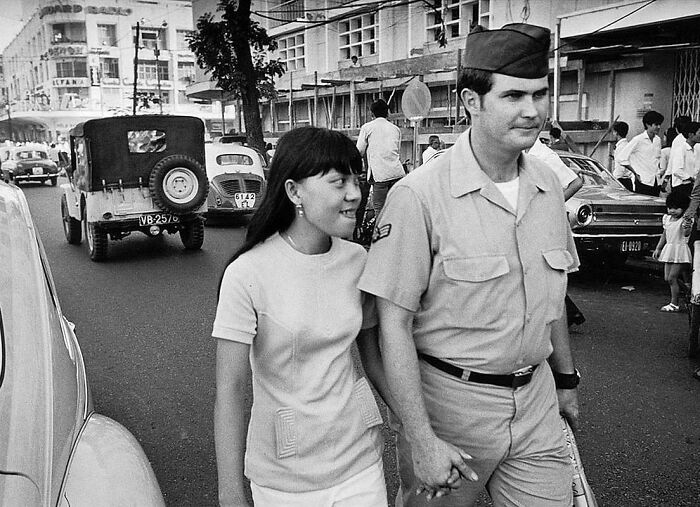 A soldier and a woman holding hands on a busy vintage street, capturing a historical moment.