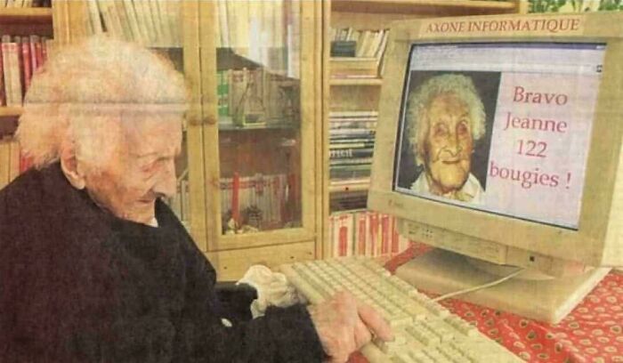 Elderly woman at computer celebrating 122nd birthday, highlighting a historical moment in a library setting.