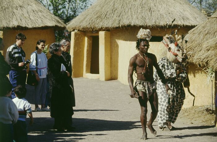 People in traditional attire with tourists in an African village, showcasing historical cultural experiences.