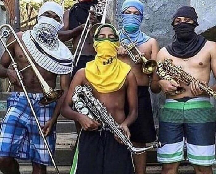 Shirtless individuals with faces covered, holding brass instruments in a random, cursed image setting.