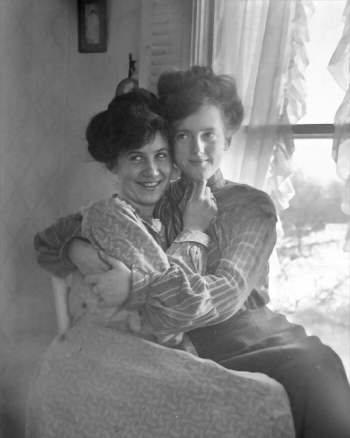 Two women in vintage clothing pose closely, embodying historical charm.
