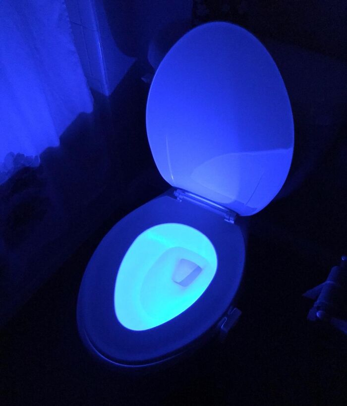 Smart home toilet with glowing blue LED light in a dark bathroom.