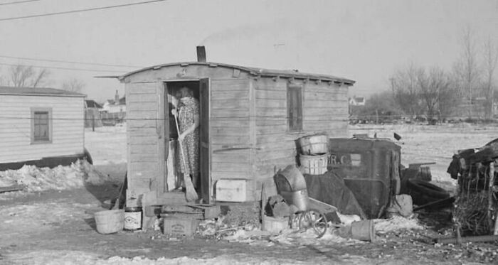 A person steps out of a small wooden shack in a snowy landscape, offering a glimpse into historical living conditions.