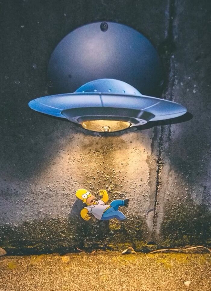 Simpsons paper cutout of Homer under a UFO light in a real-world setting.